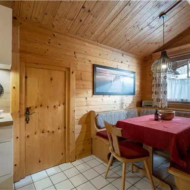 A cozy wooden room with a red table and benches. The atmosphere is warm and inviting, ideal for social gatherings.