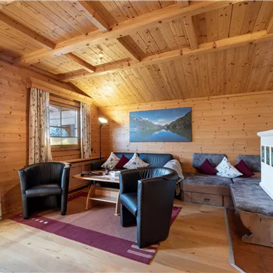 A cozy living space with wood paneling and a large window. There are comfortable seating options and a table in a warm atmosphere.