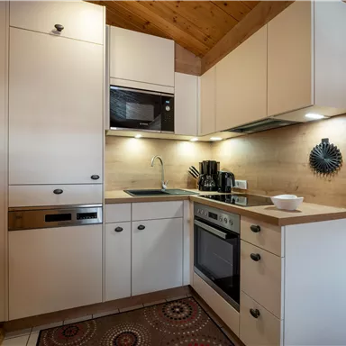 A modern kitchen with white cabinets and wooden accents. It is compact and well-equipped with various appliances.