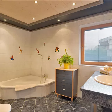 A modern bathroom with a bathtub and a shower. There is a plant and colorful wall stickers for children.