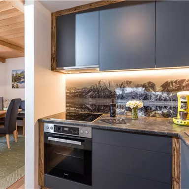 A modern kitchen with elegant dark cabinets and a beautiful countertop. In the background, a stylish mountain landscape can be seen, while a yellow coffee machine accents the room.