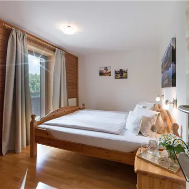 A bright bedroom with a large bed and wooden paneling. Curtains let light in, and there are some decorative pictures on the wall.