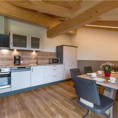Eine moderne Küche mit Holzdecken und hellen Möbeln. Ein Essbereich mit gedecktem Tisch und Pflanzen auf einem Sideboard.