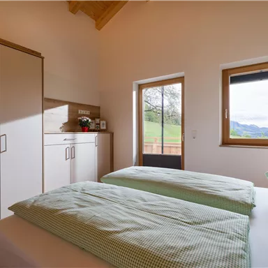 Ein gemütliches Schlafzimmer mit zwei Einzelbetten und grün karierten Bettbezügen. Durch das Fenster ist eine schöne Aussicht auf die Landschaft zu sehen.