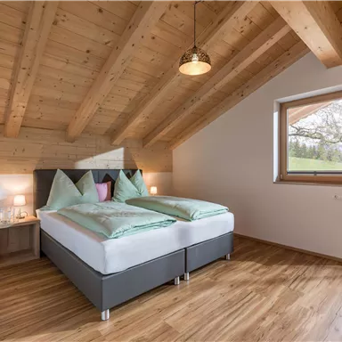 Ein modernes Schlafzimmer mit einem Doppelbett und Holzdecke. Große Fenster bieten einen Blick ins Freie.