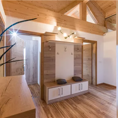 Ein heller Eingangsbereich mit Holzverkleidung und natürlichem Licht. Es gibt eine Garderobe mit Sitzgelegenheiten und Pflanzen.