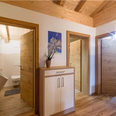 Ein heller Flur mit Holzwänden und mehreren Türen, die zu den Räumen führen. Ein kleiner Schrank steht in der Mitte, und eine Pflanze sorgt für einen schönen Akzent.