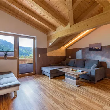 Ein modernes Wohnzimmer mit Holzdecke und großen Fenstern. Es ist hell und freundlich, mit einer gemütlichen Couch und einem Tisch.