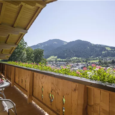 A beautiful balcony with a view of the mountains and the city. The balcony is equipped with blooming plants and furniture.