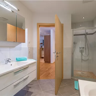 A modern bathroom with a shower and a sink. There are bright colors and wooden details that create an inviting atmosphere.
