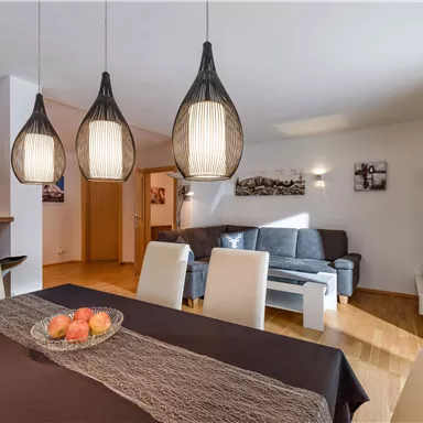 A modern living room with a dining table and elegant lamps. In the background, a cozy seating area can be seen.