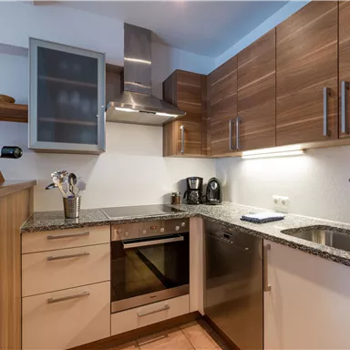 A modern kitchen with wooden cabinets and a granite countertop. It is equipped with appliances such as a stove and a dishwasher.