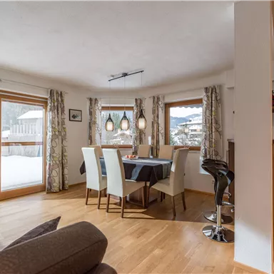 A bright dining room with a table and chairs. Large windows let in a lot of light and offer a view of the wintry landscape.