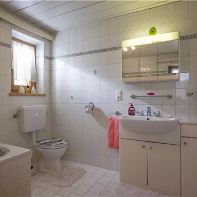 A bright bathroom with white tiles and a large mirror. There is a bathtub, a sink, and a toilet area.