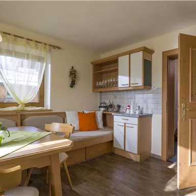 A bright kitchen with a dining table and a cozy seating area. The walls are designed in warm colors and the windows let in plenty of natural light.