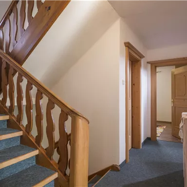A staircase with a wooden railing and blue carpet. There are several doors leading to different rooms.