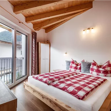 Ein gemütliches Schlafzimmer mit einem großen Bett und karierten Bettdecken. Helle Wände und ein Holzdecke schaffen eine einladende Atmosphäre.
