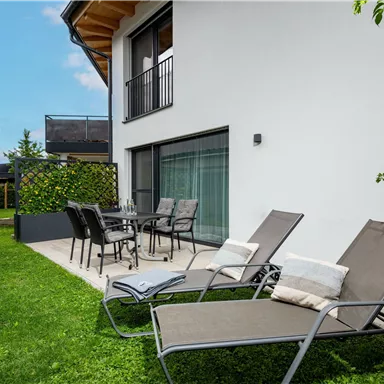 Ein moderner Gartenbereich mit zwei Liegen und einem Esstisch. Das Gebäude ist hell und lädt zum Entspannen ein.
