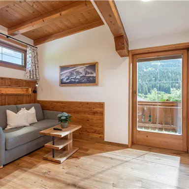 A cozy room with wooden paneling, a sofa, and a small table. Large windows offer a view of the nature outside.