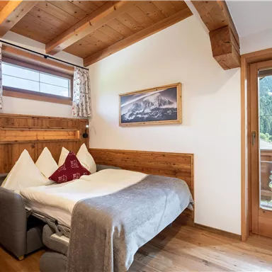 A cozy bedroom with wooden details and a double bed. A window offers a view of the mountains and the garden.