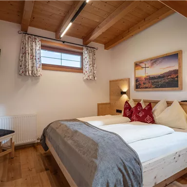 A cozy bedroom with two beds, wooden details, and a TV. Large windows let in plenty of light and create a pleasant atmosphere.
