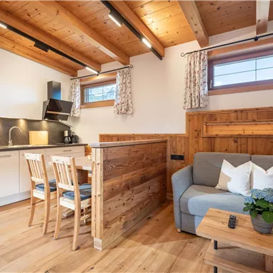 Cozy living space with an open kitchen and wooden furniture. The room is bright and inviting, with natural light coming through the windows.