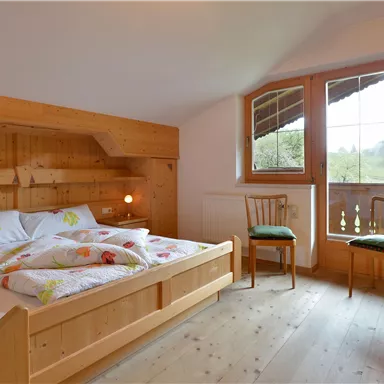 A cozy bedroom with wooden decor and a large window. There is a double bed and two chairs that create an inviting atmosphere.