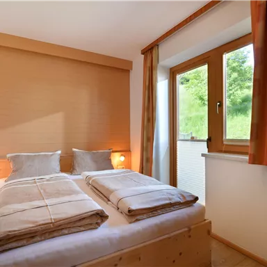 Ein gemütliches Schlafzimmer mit zwei Betten und warmen Farben. Ein Fenster sorgt für viel Tageslicht und Blick ins Grüne.