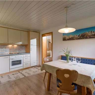 A cozy dining area with a modern kitchen. The table is beautifully set and there is a large window front with a view of the mountains.