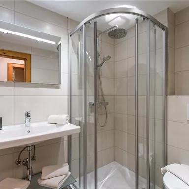 A modern bathroom with a glass shower, a sink, and a large mirror. The walls are brightly tiled and there are towels nearby.