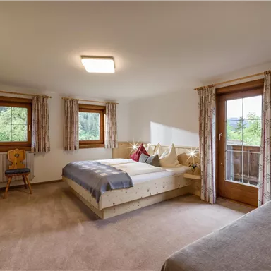 An inviting bedroom with a double bed and a single bed. Large windows ensure plenty of light and provide a view of the greenery.