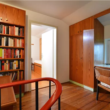 A cozy study with a bookshelf and a desk. The room has wood-paneled walls and a window with a view outside.