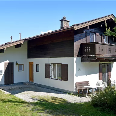 A cozy house with a balcony in a rural setting. The meadow is green and the sky is clear.
