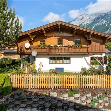 Ein traditionelles Haus mit Holzverkleidung in einer malerischen Landschaft. Umgeben von einem gepflegten Garten und Blick auf die Berge.