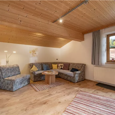 Ein gemütliches Wohnzimmer mit einer modernen Couch und einem Holztisch. Große Fenster lassen viel Licht herein und sorgen für eine einladende Atmosphäre.