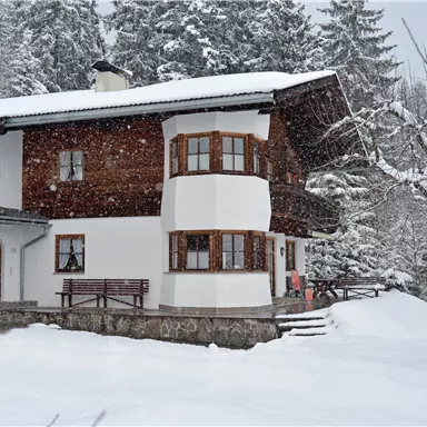 A charming house in the snow, surrounded by snow-covered trees. The scene conveys a tranquil winter atmosphere.