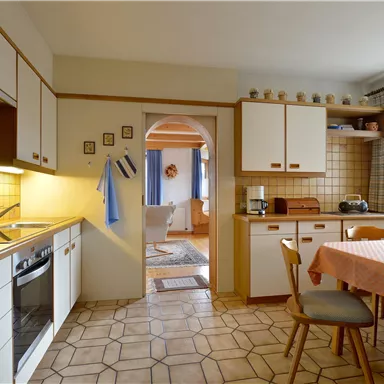 A bright kitchen with white cabinets and a dining area. The room is friendly furnished and has an open access to the living room.