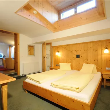 A cozy bedroom with wooden decor and two beds. The room has natural light sources and an inviting atmosphere.