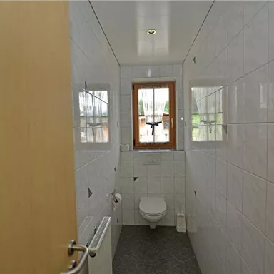 A simple bathroom with white tiles and a window. It includes a toilet and a heater.