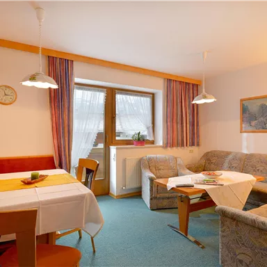 A cozy living room with a seating area and a dining table. Bright colors and a window create an inviting atmosphere.