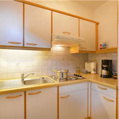 A modern kitchen with bright cabinets and a countertop. On the counter, there is a pot and a coffee machine.