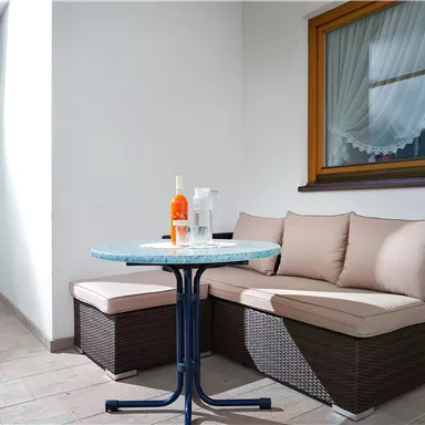 A cozy balcony with a round table and a couch. Drinks are on the table to create a relaxed atmosphere.