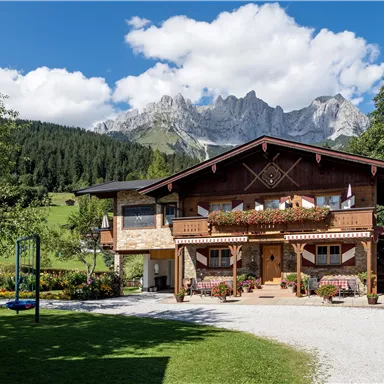 Ein charmantes alpenländisches Haus vor einer beeindruckenden Bergkulisse. Der Garten ist gepflegt und erhöht die ländliche Atmosphäre des Ortes.