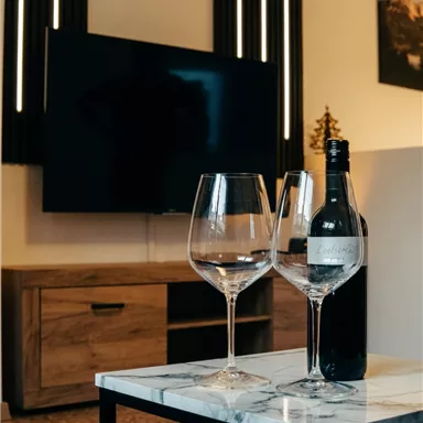 An elegant living room with a television and a wooden table. On the table, there are two wine glasses and a bottle of wine.