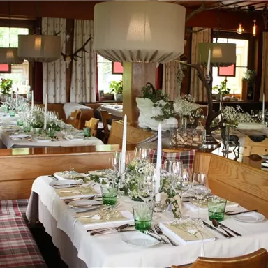 A stylishly furnished restaurant with two set tables. The tables are decorated with flowers, glasses, and candles to create a cozy atmosphere.