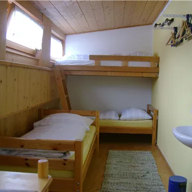 A simple room with two bunk beds and a single bed. There is a small washing area and plenty of daylight through the windows.