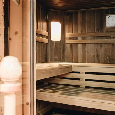 A modern wooden sauna with benches and a clock on the wall. The light gently falls through the window, creating a relaxing atmosphere.