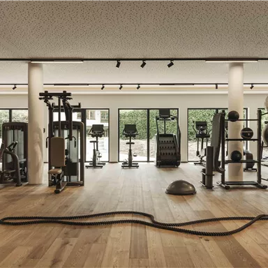 Ein modernes Fitnessstudio mit verschiedenen Trainingsgeräten und einem hellen, einladenden Ambiente. Große Fenster bieten Blick auf den Außenbereich.