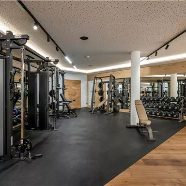 Ein modernes Fitnessstudio mit verschiedenen Geräten und Freihanteln. Der Raum hat eine helle, einladende Atmosphäre und einen Holzfußboden.