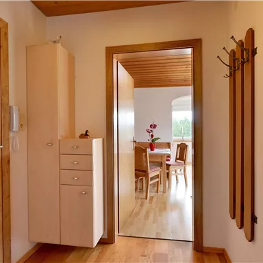 Ein heller Flur mit Holzfußboden und einem Schrank. Im Hintergrund ist ein Essbereich zu sehen.